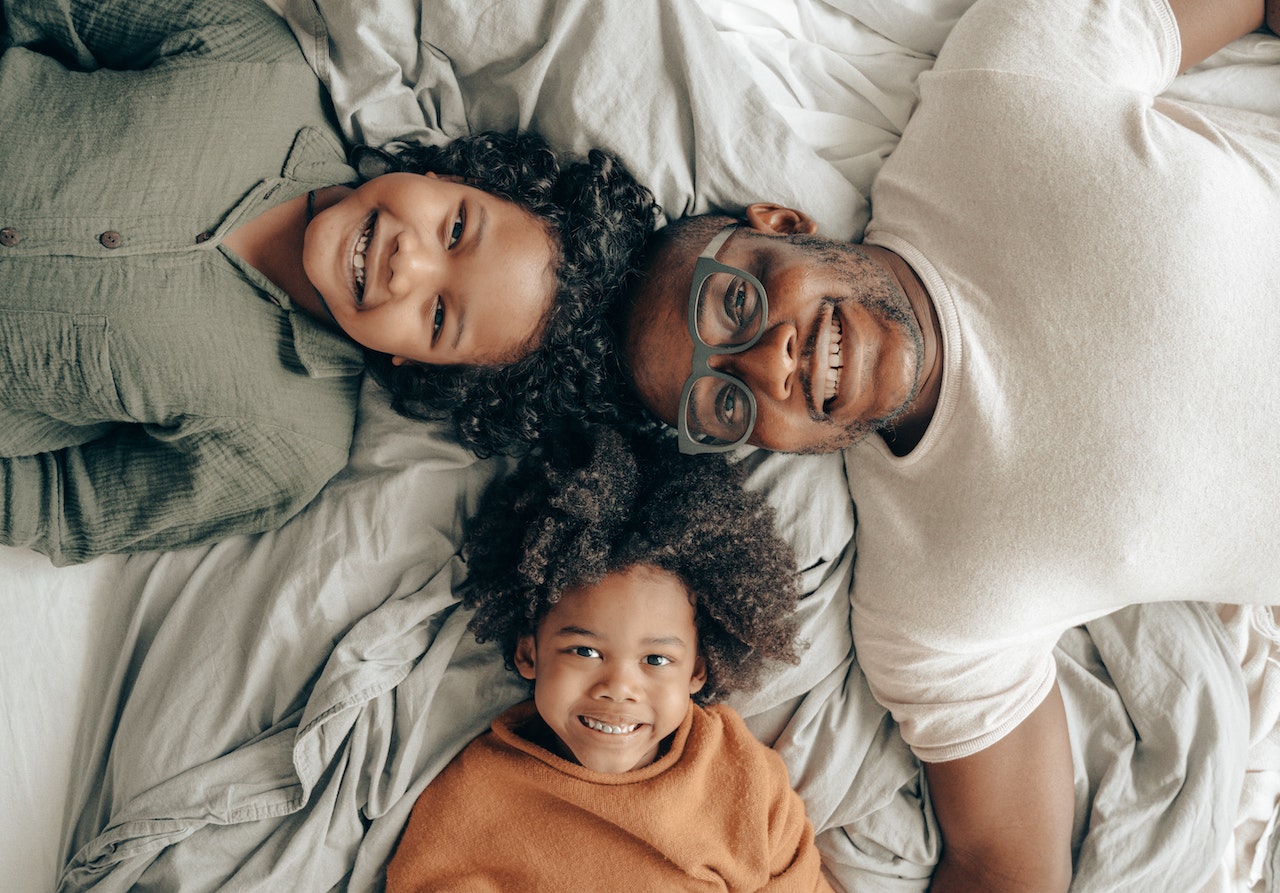 a dad and two kids smiling on a bed