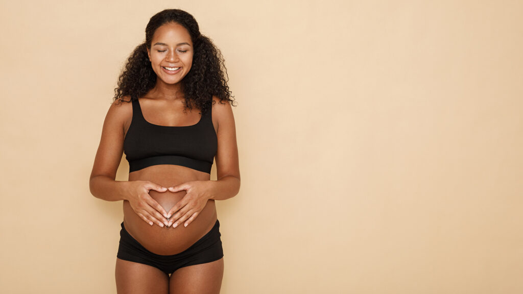 Pregnant woman holding hands on her belly making a heart symbol