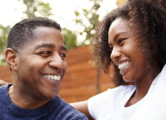 Middle aged black dad and teenage daughter smiling at each other, close up
