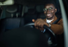 Cheerful young African American man enjoys driving his car.