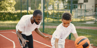 Black father with son playing basketball in basketball court together