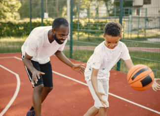 Black father with son playing basketball in basketball court together