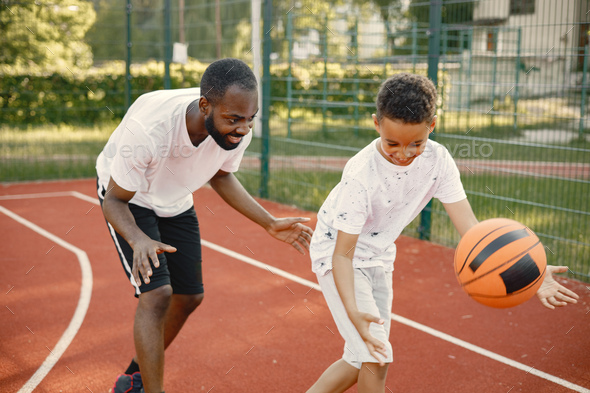 Black father with son playing basketball in basketball court together