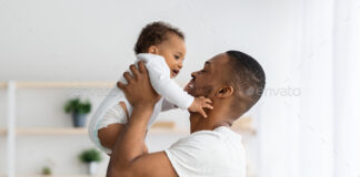 Father's Day Concept. Loving Young Black Dad Lifting Up Cute Infant Baby
