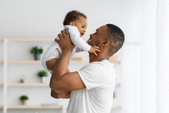 Father's Day Concept. Loving Young Black Dad Lifting Up Cute Infant Baby