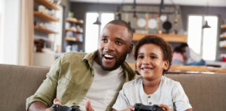 Father And Son Sitting On Sofa In Lounge Playing Video Game